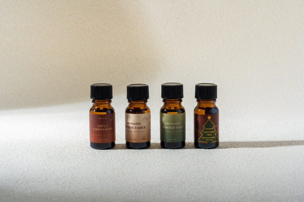 Four Aromadd 10 ml fragrance oil sample bottles on a sunlit cream surface.