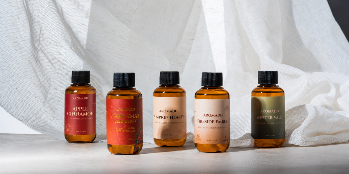 Five Aromadd holiday diffuser oils—Apple Cinnamon, Christmas Cranberry, Pumpkin Hearth, Fireside Ember and Winter Vale—on a light surface.