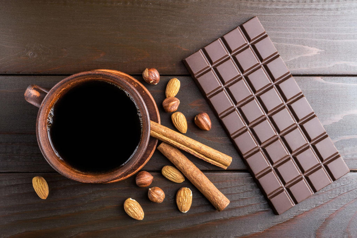 Coffee, chocolate, nuts and cinnamon arranged on a wooden surface.